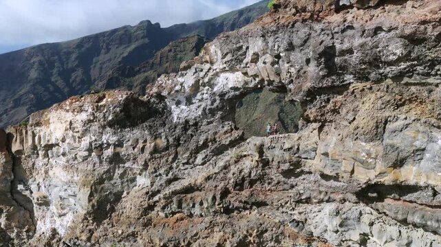 Hiking couple sitting inside El Bujero rock cave overlooking Los Gigantes cliffs and Masca Valley in Tenerife