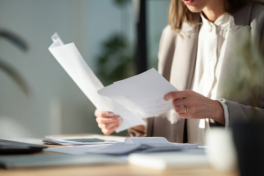 Close-up of businesswoman reviewing financial documents at desk, focused expression, natural daylight highlighting details, professional calm environment