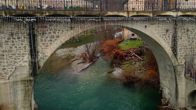 Dolly Zoom Drone Flight Over Capuchin Bridge: Vertical Reveal from Water, Ancient Stone Arch in Skofja Loka Medieval Town Slovenia, Creative Cinematography, Historic Landmark 4K