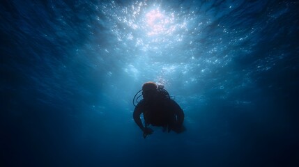 A lone scuba diver descends into the deep blue ocean illuminated by shimmering sunlight filtering from the surface