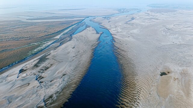 An aerial view shows a narrow channel of the Brahmaputra River cutting through vast exposed sandbanks during the dry season in Majuli, Assam.