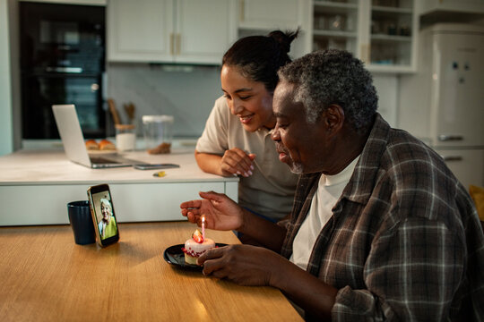 Daughter and senior man celebrating birthday by video call in home kitchen