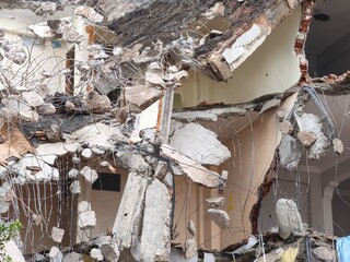 Exposed Rebar and Concrete Hanging from Partially Demolished Building. Dangerous Demolition Scene with Swinging Rebar and Rubble. Collapsed Structure with Hanging Metal and Concrete Fragments.