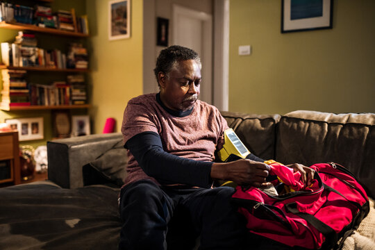 Mature man packing a red duffel bag on living room sofa