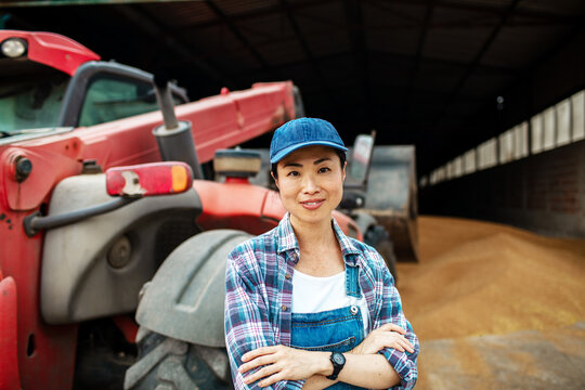 Confident female farmer with tractor in grain storage barn