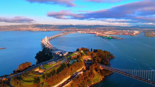 San Francisco Bay Bridge connecting the main span to Yerba Buena Island. The Port of Oakland is visible in the background across the water. Aerial view