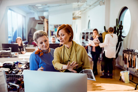 Female fashion designers collaborating at computer in modern studio
