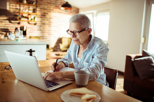 Senior woman working on laptop in cozy home kitchen