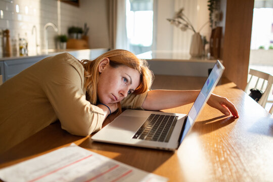 Tired woman working on laptop at home kitchen table