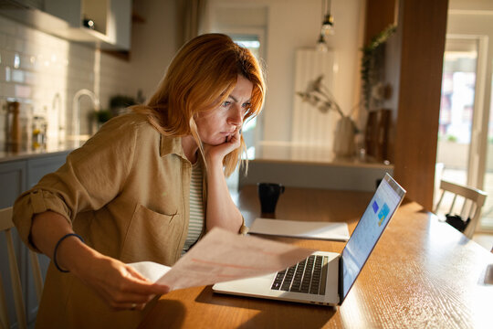 Concerned woman reviewing bills on laptop at kitchen table