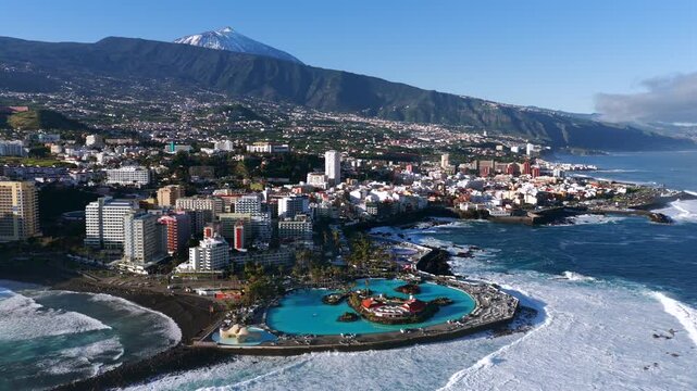 Cinematic aerial sunrise over Puerto de la Cruz cityscape with Lago Marti&aacute;nez and Teide volcano in Tenerife