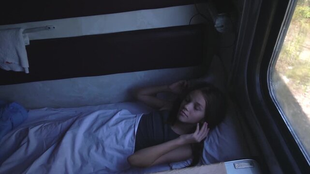 A girl lies on a train shelf with bed linen spread out and rests while traveling in her compartment during a train ride. High quality FullHD footage