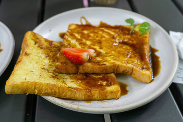 Delicious Caramel French Toast Topped with Fresh Strawberry and Mint Leaf Garnish on a White Plate © Jaenal Jalalludin