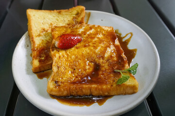 Delicious Caramel French Toast Topped with Fresh Strawberry and Mint Leaf Garnish on a White Plate © Jaenal Jalalludin