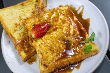 Delicious Caramel French Toast Topped with Fresh Strawberry and Mint Leaf Garnish on a White Plate © Jaenal Jalalludin