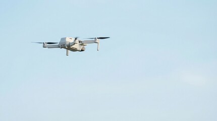 Modern grey unmanned aerial vehicle flies forward in a clear pale blue sky demonstrating aerial surveillance or photography capability.