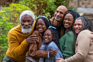 Obraz premium Diverse family including senior and children hugging in garden with stone wall, wearing sweaters