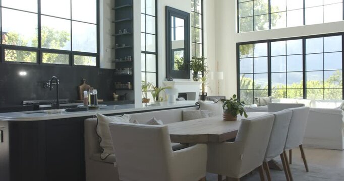 Camera is pulling back and panning right, revealing open-plan kitchen and dining area with windows