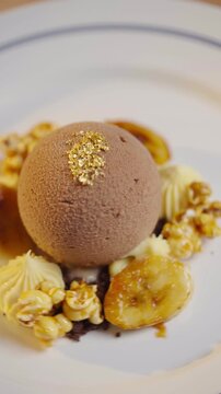A dessert with a chocolate ball on top of a plate with banana slices and chocolate chips. The dessert is served on a white plate with a blue border