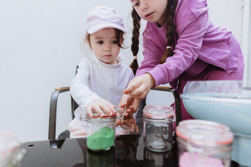 Two girls close a metal latch on a jar of green sugar.