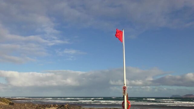 Red flag fluttering in strong wind - swimming ban, warning signal for swimmers on the beach, storm, beach safety, dangerous conditions, wind force, wind direction,  weather forecast, coast
