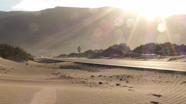 Verlassene Stra&szlig;e im Sandsturm in karger Umgebung mit prallem Sonnenschein, Hitze, Einsamkeit, Landschaft, Umwelteinfl&uuml;sse, Natur, Klima, Reisen, Abenteuer, Atmosph&auml;re, Verkehr, Kanaren, Lanzarote