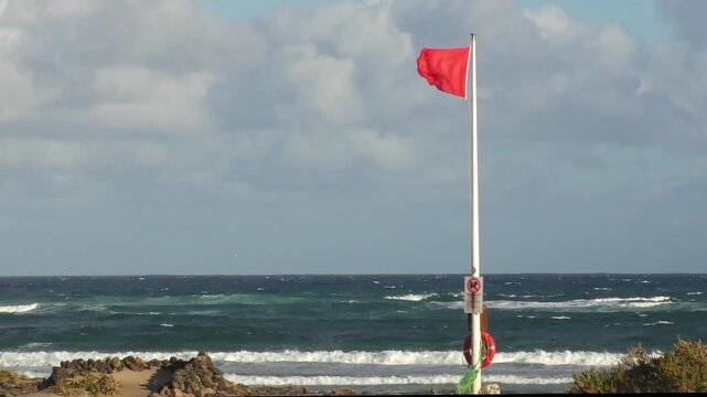 Red flag fluttering in strong wind - swimming ban, warning signal for swimmers on the beach, storm, beach safety, dangerous conditions, wind force, wind direction,  weather forecast, coast
