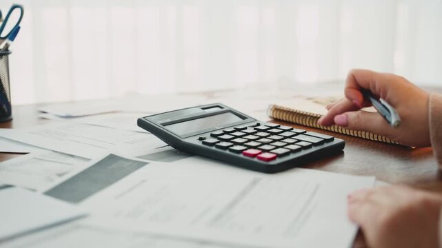Close up hand person accountant working at desk using calculator planning corporate budget. Stressed woman taking notes checking utility bills taxes data bank account balance. out-of-pocket expenses