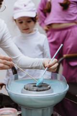 A teenage girl and her sisters spoon blue sugar into a cotton candy machine.