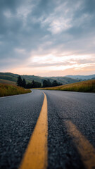 Dramatic asphalt road winding through peaceful rolling hills towards cloudy sky during sunset view from low ground perspective featuring yellow line and journey concept