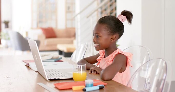 Child reacting to online lesson starting, sitting at dining table speaking to join on laptop