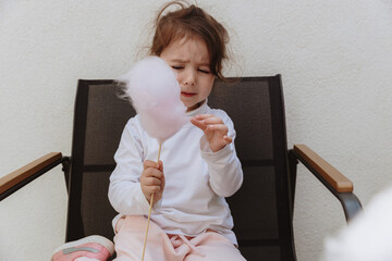 A little girl eats cotton candy on a stick in the garden.