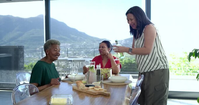 Diverse women at table standing woman pouring wine serving salad starting meal mountain view