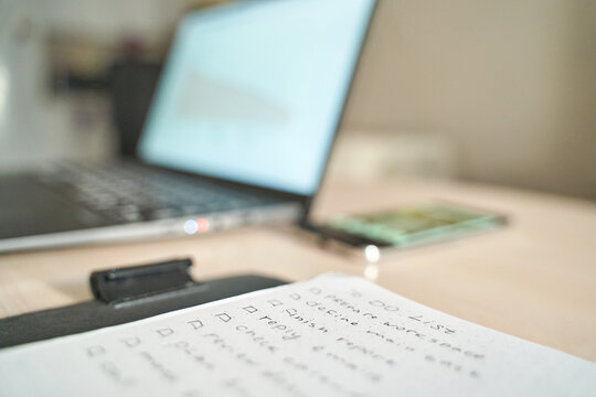 Close-up of notebook with to-do list next to laptop and phone on desk in office setting.
