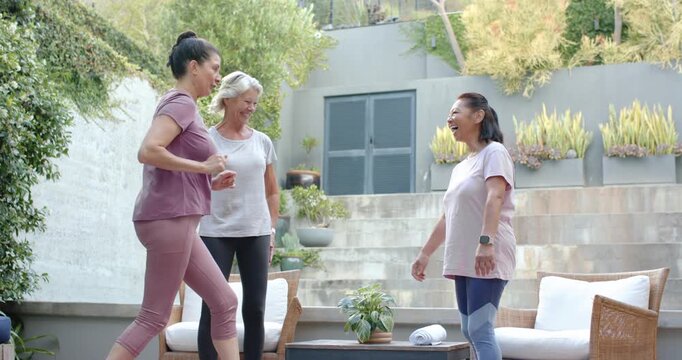 Diverse women with senior in activewear approaching raising hand greeting high fives hugs on patio