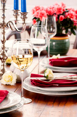Festive decorated laid table with silver sterling cutlery, candle holder, porcelain tableware, glasses and flowers