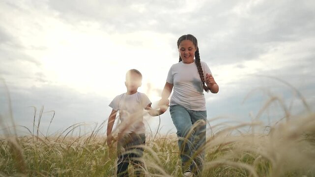 Children holding hands while running in field. Girl and boy laugh together. Child runs through grass. Kid running with sibling. Holding hands helps children stay close. Field running with joy.