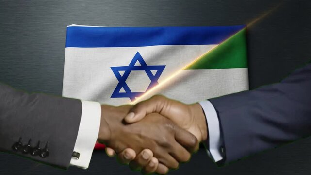 Two businessmen shake hands firmly against the backdrop of blended Israeli and Sudanese flags symbolizing diplomatic partnership and peace efforts.