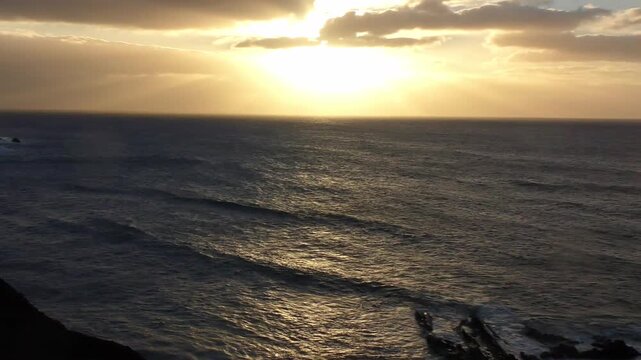 atemberaubender Sonnenuntergang &uuml;ber dem Meer hinter dramatischen Wolken - brechenden Wellen im Abendlicht an felsiger K&uuml;ste, beruhigende Stimmung, inspirierende Landschaft, Reisen, Urlaub
