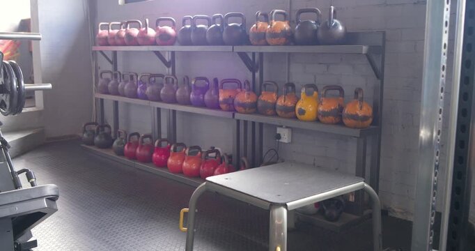 Handheld camera is panning left-right, revealing kettlebell rack and bench to showcase compact gym