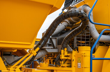Close-up of a hydraulic hose system and cooling radiator on a yellow mining dump truck. Heavy industrial machinery components, hydraulic lines with protective sleeves on a massive vehicle. © NastyaPhoto