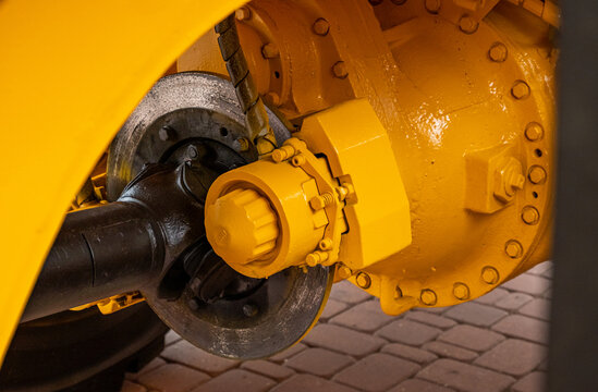 Close-up of a heavy-duty truck axle and disc brake system on yellow industrial machinery. Detailed view of the cardan shaft, differential housing, and braking mechanism for construction equipment.