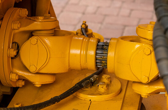 Close-up of a heavy-duty cardan shaft and splined connection on yellow industrial machinery. Detailed view of a drivetrain universal joint and hydraulic lines on a construction loader chassis.