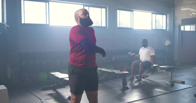 African American men warming up at gym, adjusting sleeve and checking watch, partner doing reps