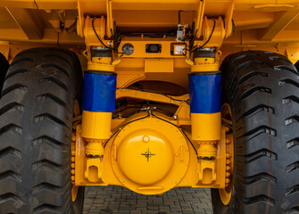 Rear view of a massive yellow mining dump truck axle and suspension system. Close-up of industrial vehicle heavy-duty tires, hydraulic cylinders with blue covers, and differential housing. © NastyaPhoto