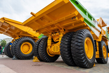 Rear view of massive yellow and green mining dump trucks at an exhibition. Industrial heavy-duty vehicles with giant tires, hydraulic suspension, and powerful axles for quarry operations. © NastyaPhoto