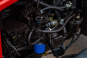 Close-up of a modern red tractor diesel engine with fuel system and filters. Detailed industrial view of a professional agricultural vehicle motor and components for farming machinery.