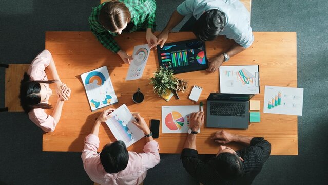 Top view of diverse business people working together to analyze chart. Top down aerial view of creative team looking at stock market report and discussing about financial investment. Convocation.