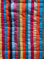 Fototapeta premium Hand-dyed cotton stripes arranged in lively array of colors, pieced and hand- quilted into this striking textile composition.