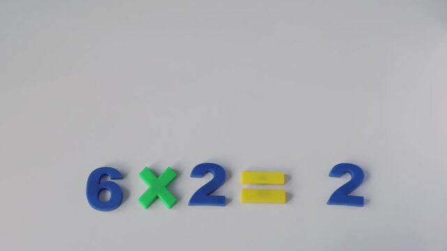 Mathematics education and learning, hand placing plastic number twelve to complete multiplication equation on white background
